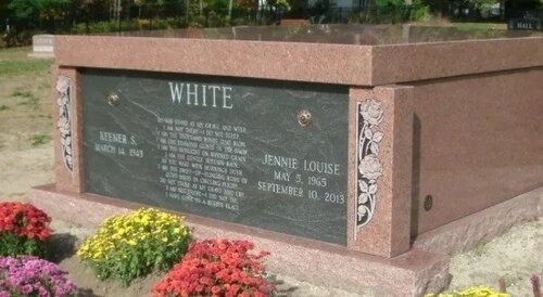 Brown memorial tomb with “WHITE” engraved, surrounded by flowers in a cemetery.