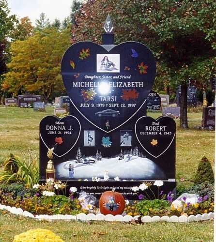 Decorative heart-shaped memorial headstone in a cemetery, black with flowers and white lettering.