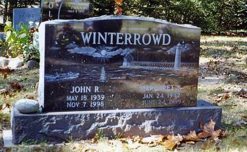 Dark granite gravestone engraved “WINTERROWD” in a cemetery with leaves and flowers around it