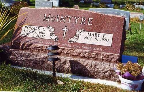 Red granite McIntyre gravestone with cross and flower vases in a cemetery.