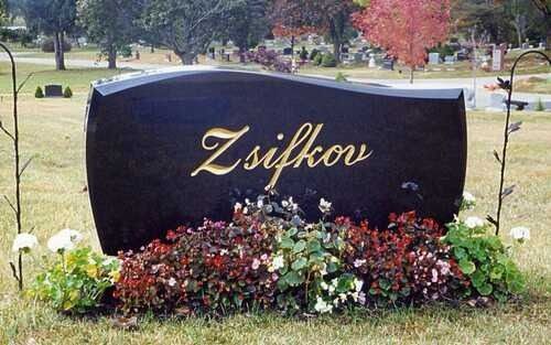 Black memorial stone engraved “Zsifkov,” surrounded by flowers in a cemetery garden