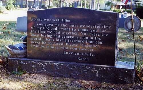 Black memorial plaque with white inscription on a low stone base in a cemetery or park setting