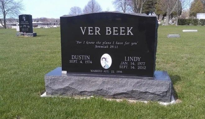 Black granite cemetery headstone reading “VER BEEK” on a grassy lawn under a bright sky.