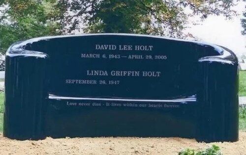 Black curved memorial headstone with engraved names and dates in a cemetery