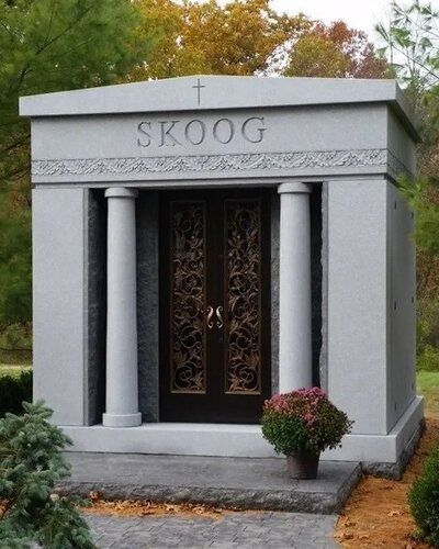 Stone mausoleum with the name SKOOG and a decorative black door, framed by columns and flowers