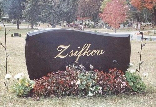 Black memorial stone engraved “Zsifkov,” surrounded by flowers in a cemetery lawn