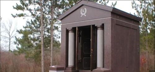 Small brown mausoleum or memorial structure in a wooded outdoor setting