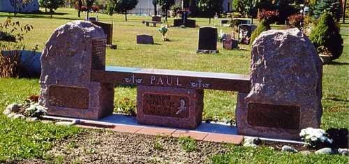 Stone memorial bench in a cemetery with a central plaque and two large engraved rocks