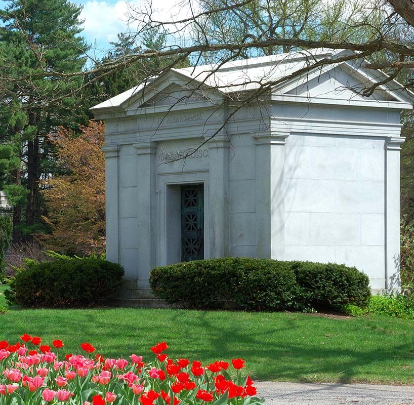 White stone mausoleum in a green park with red flowers in front