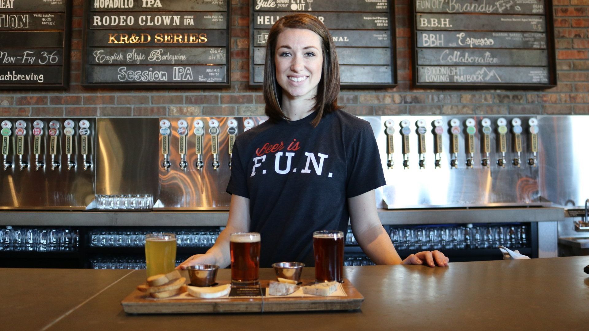 A woman is standing at a bar holding a tray of beer.