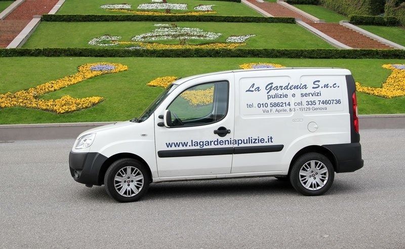 Furgone bianco con il logo aziendale parcheggiato di fronte a un prato verde decorato con fiori.