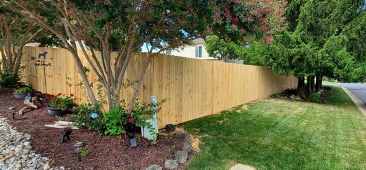 A wooden fence is surrounded by trees and rocks on the side of a road.