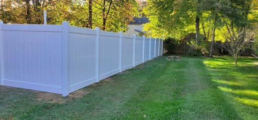 A white vinyl fence is sitting in the middle of a lush green yard.