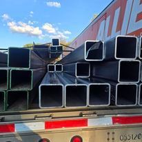 A truck filled with stacks of square metal pipes.