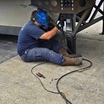 A man is sitting on the ground welding a trailer.