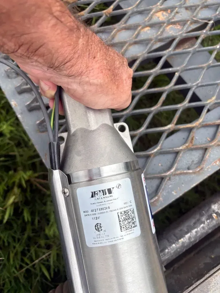 Hand holding a gray metal tool with a label over a metal mesh table outdoors