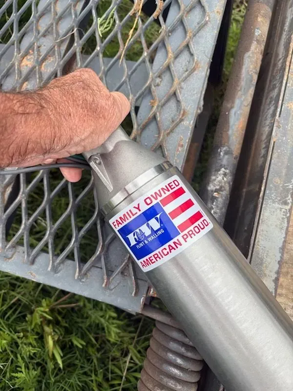 Hand holding a silver American Pride family-owned metal tool on a gray grating outdoors