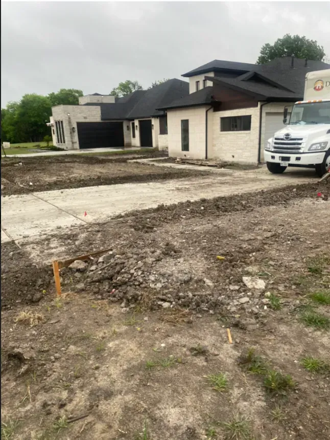Partly built house with white SUV parked beside a muddy, unfinished lot