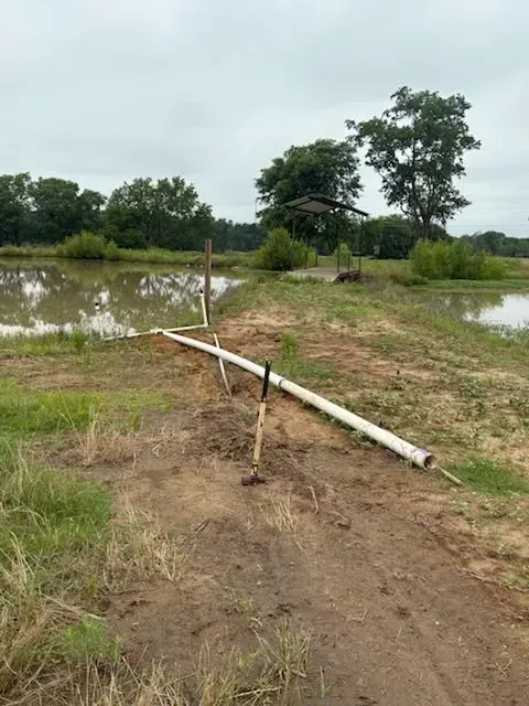 Flooded dirt path with a makeshift wooden barrier beside muddy water and trees.