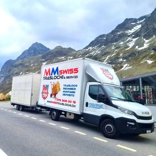 Un camion in movimento percorre una strada con le montagne sullo sfondo.