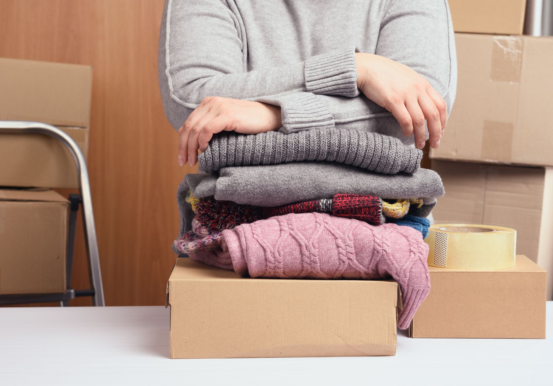 Una donna è seduta a un tavolo con una pila di vestiti sopra una scatola di cartone.