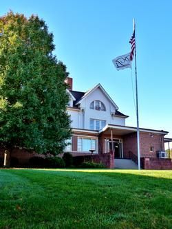 Two-story brick building with a green lawn and flagpole flying an American flag and a banner; blue sky.
