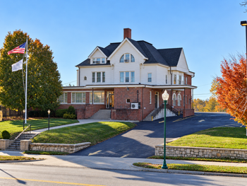 Building with American flag and sign. Two-story structure, lawn, brick and light-colored siding, under blue sky.