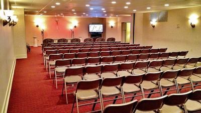 Rows of brown chairs face a small stage in a carpeted room.
