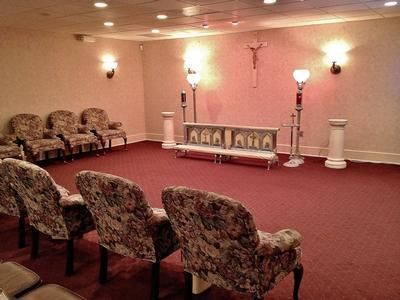 Funeral home chapel with chairs, altar, crucifix, and red carpet.