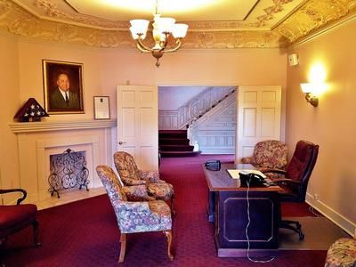 Funeral home interior with chairs, desk, fireplace, portrait, staircase.