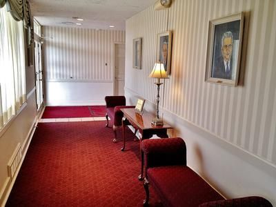 Hallway with red carpet, striped wallpaper, portraits, and benches.