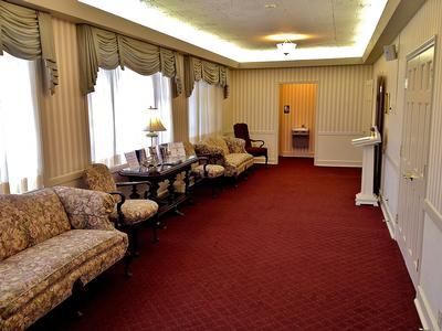 Interior of a funeral home with floral patterned couches, red carpet, and a hallway leading to a restroom.