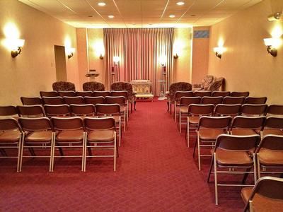 Interior of a chapel with rows of chairs, red carpet, and a curtained stage area.
