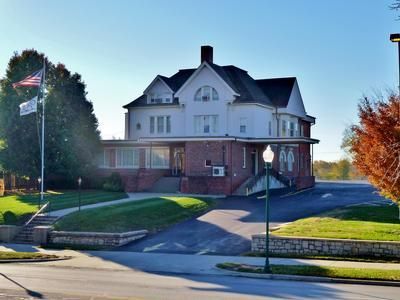 Two-story building with white siding, brick base, and large windows. US and state flags fly in front.