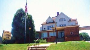 Building with American flag and sign. Two-story structure, lawn, brick and light-colored siding, under blue sky.