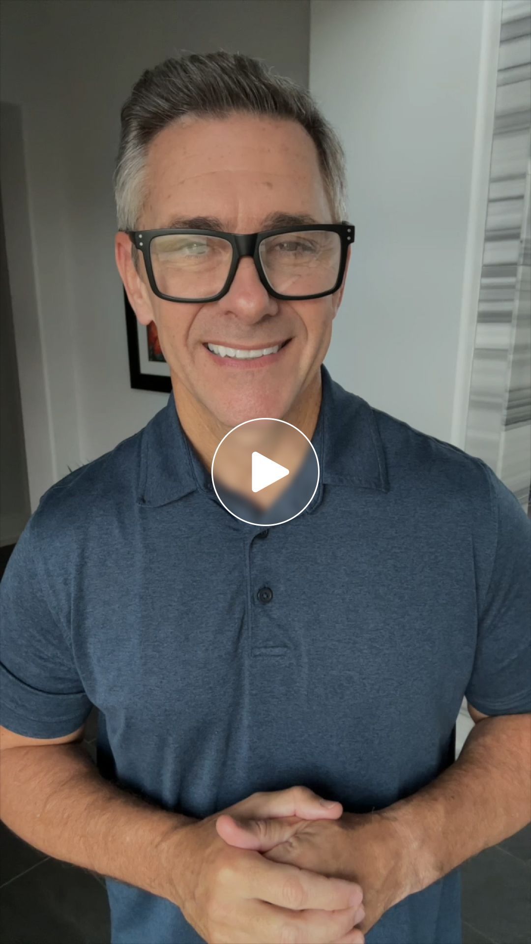 A man wearing glasses and a blue shirt is smiling.