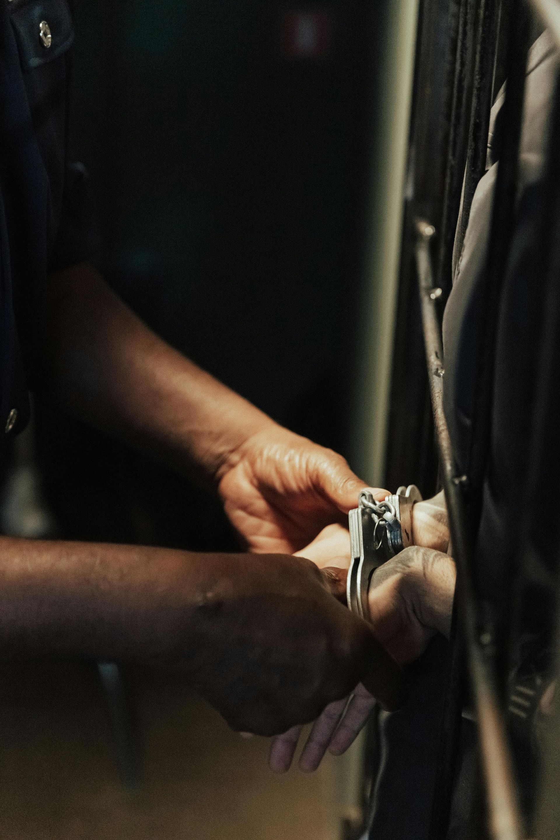 A close-up view of hands placing metal handcuffs on a person's wrists inside a dimly lit setting.