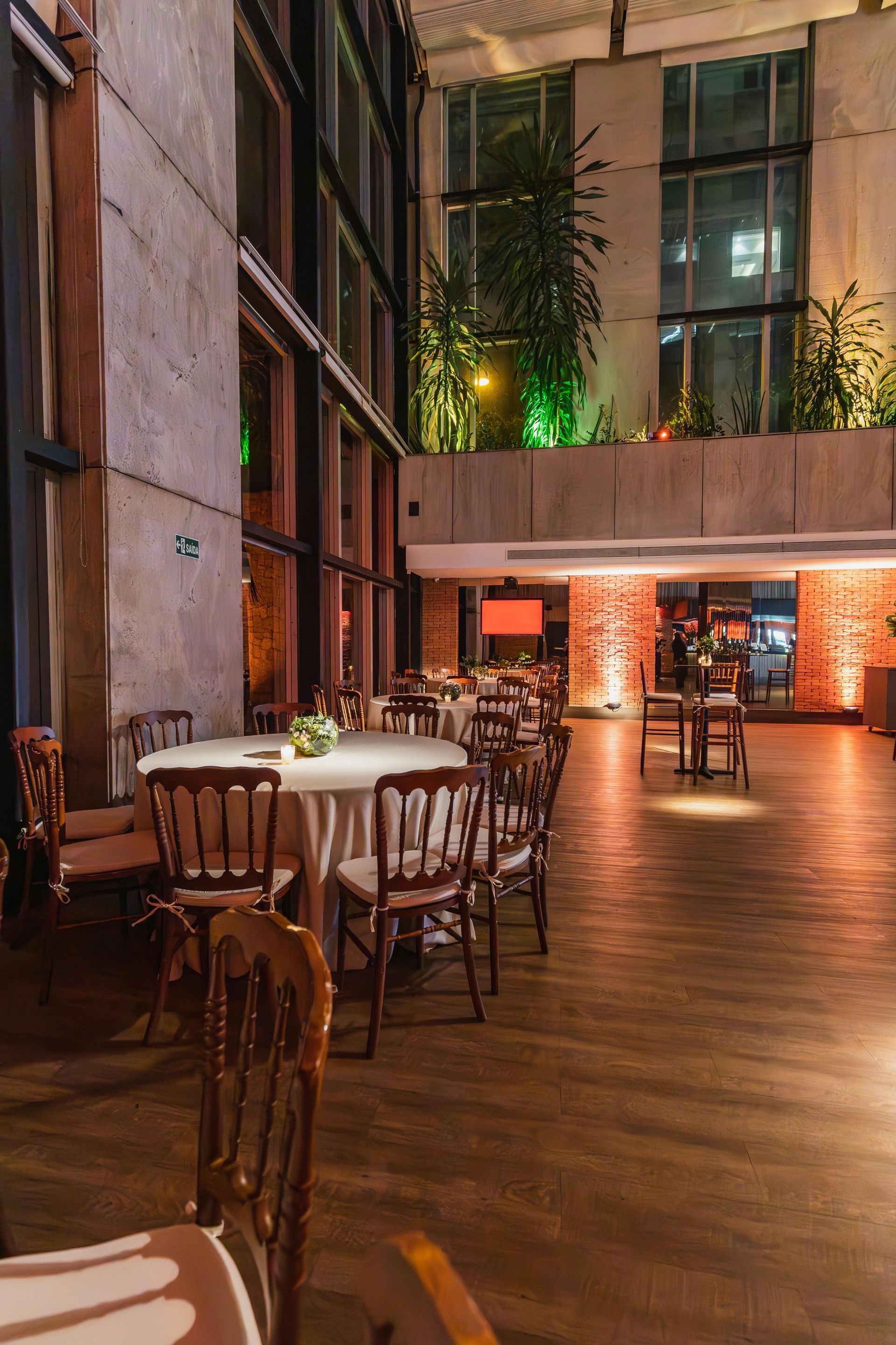 A spacious, dimly lit room arranged for an event with round tables and chairs on a wood floor, accented by warm lighting.