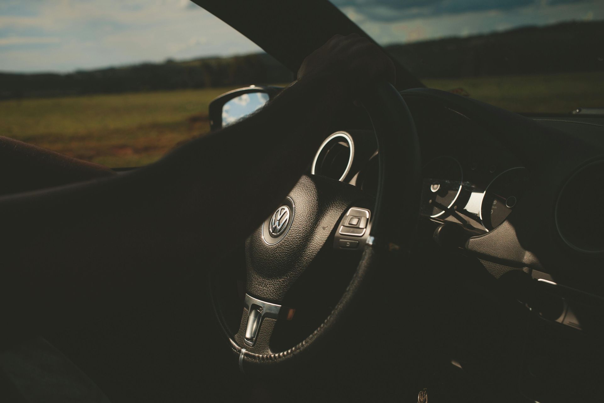 The driver's perspective from inside a car, looking out at a grassy field through the windshield and steering wheel.