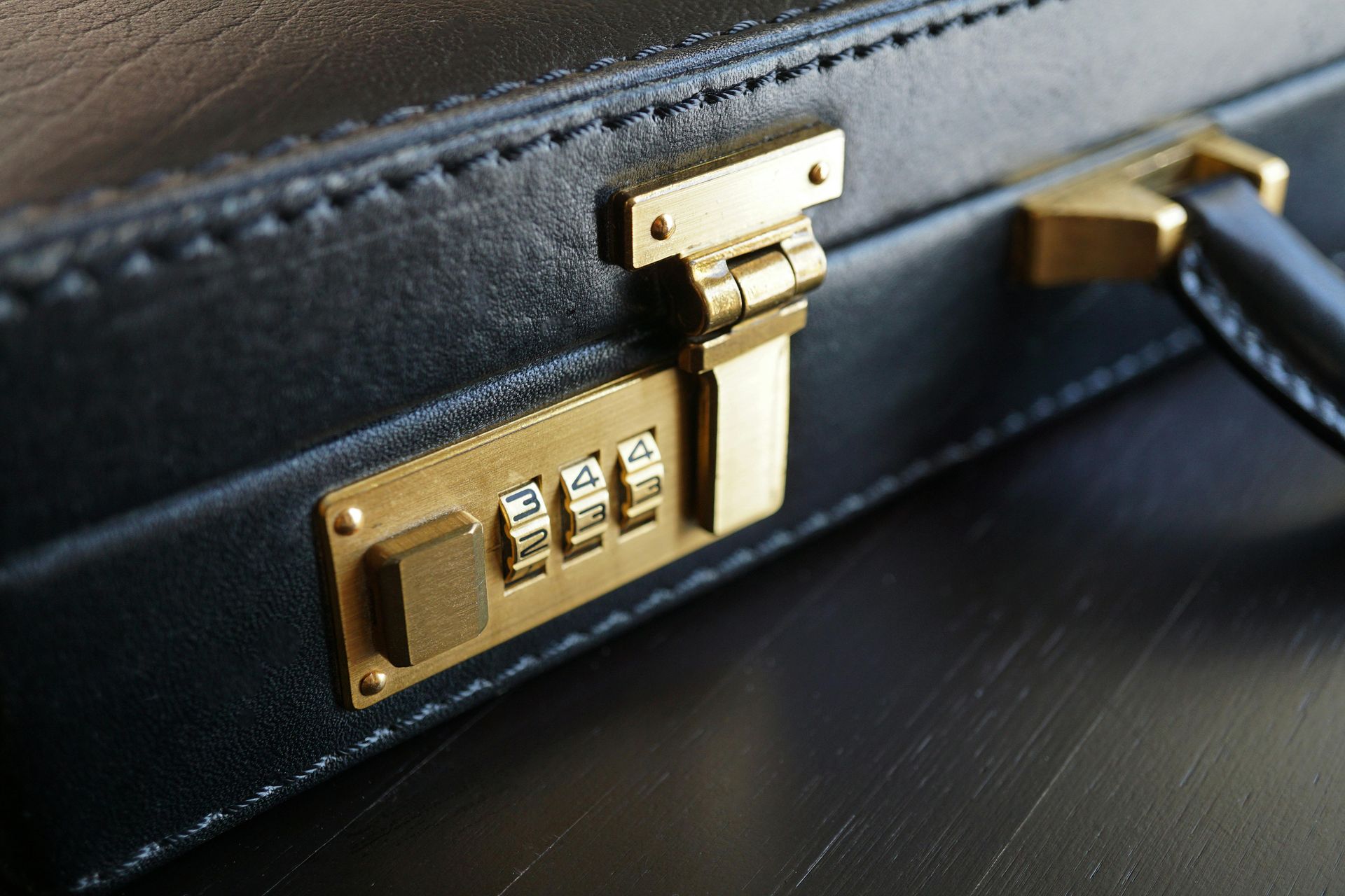 A close-up view of a black leather briefcase featuring a gold-colored combination lock and latch.