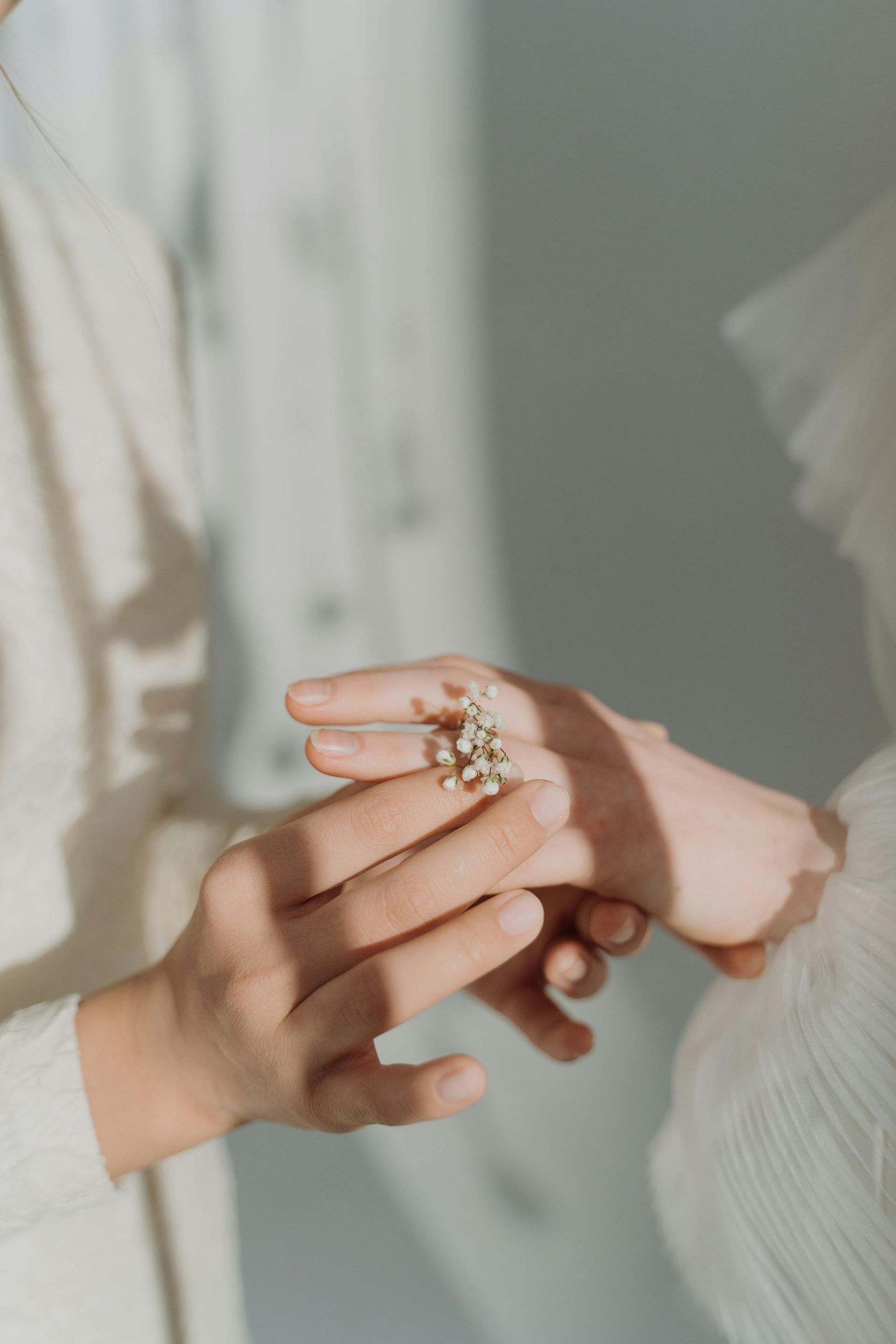 A person placing a small, white floral ring onto another person’s finger in a brightly lit, minimalist setting.