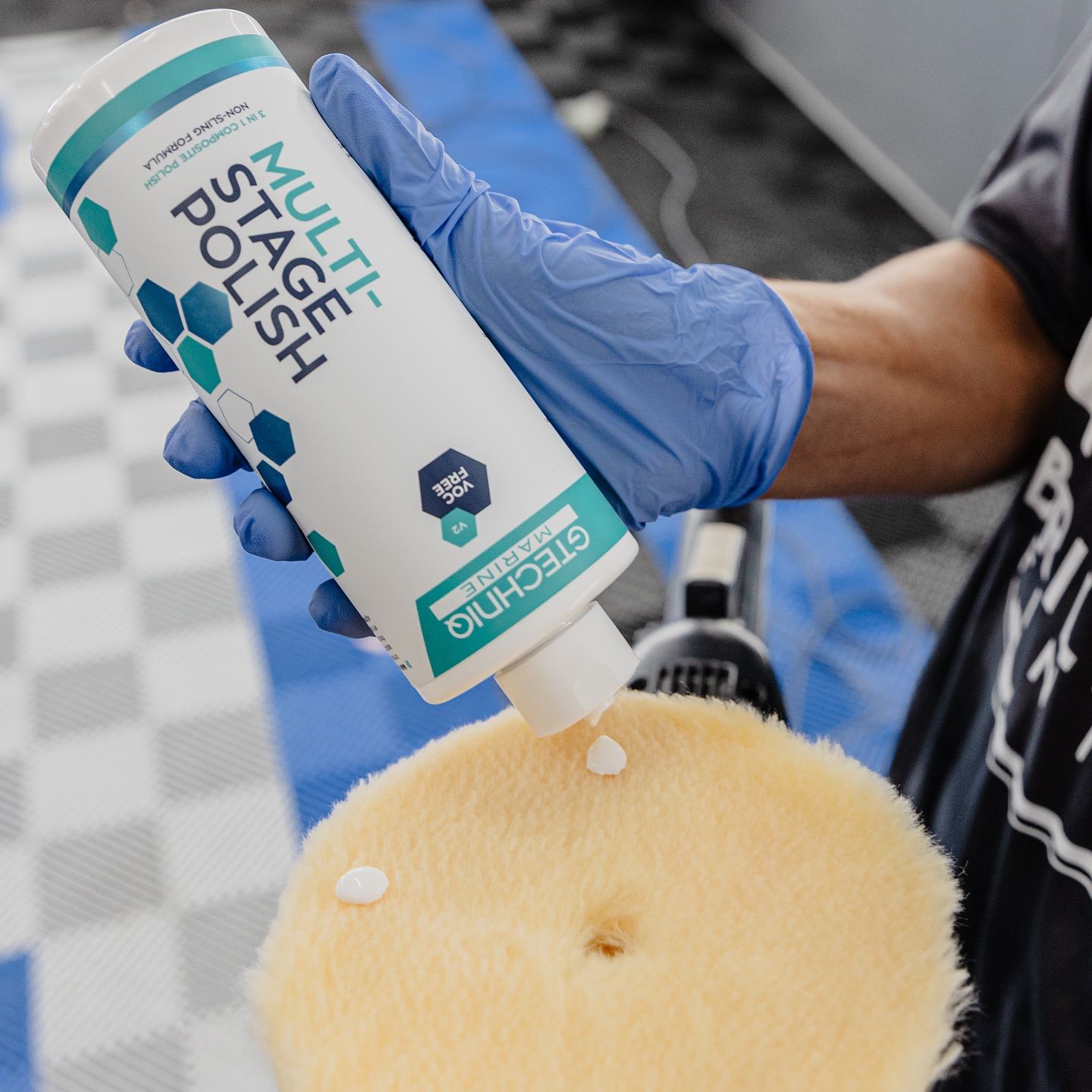 Gloved hand applying spray polish to a tan cushion with a squeeze bottle