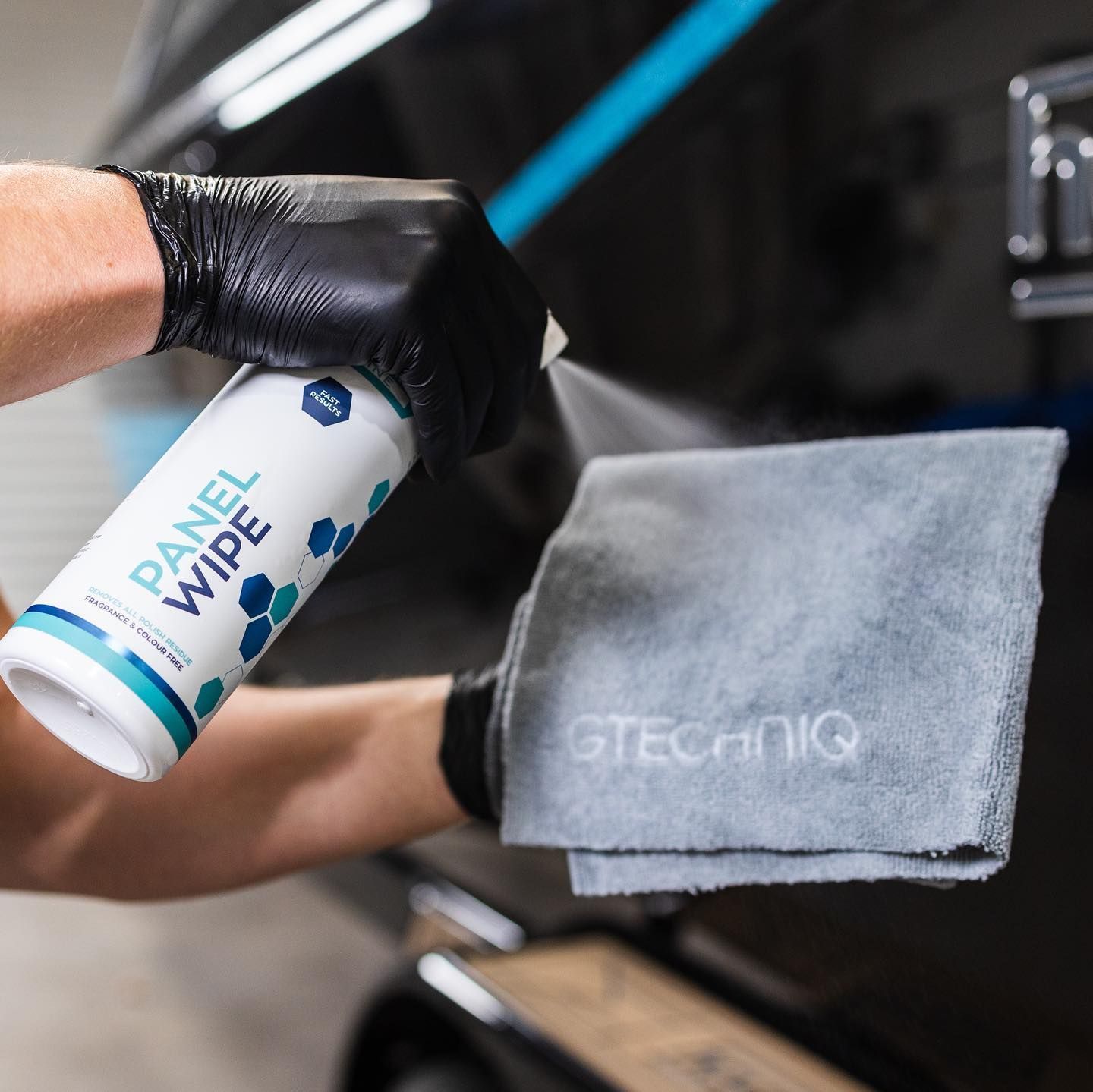 Gloved hand spraying cleaner onto a gray microfiber cloth in a car detailing setting