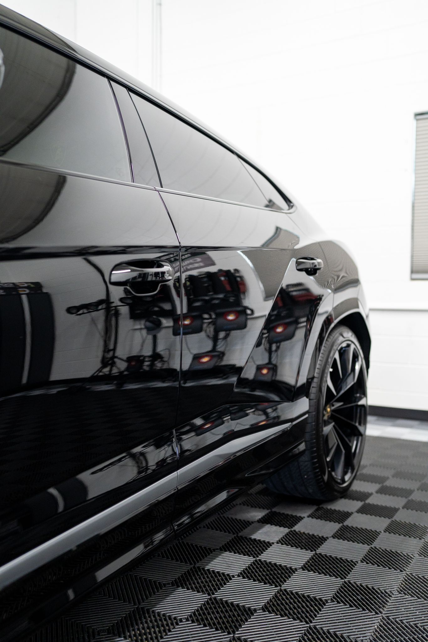 Black SUV in a bright indoor detailing bay, shown from the side on a checkered floor.