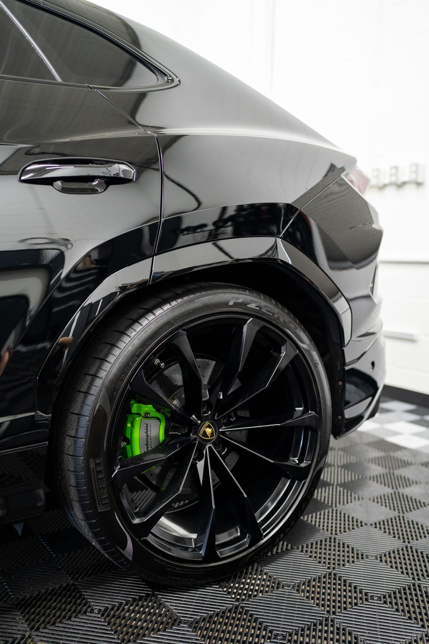 Black sports car rear wheel and fender in a detailing bay, with glossy paint and bright green brake caliper