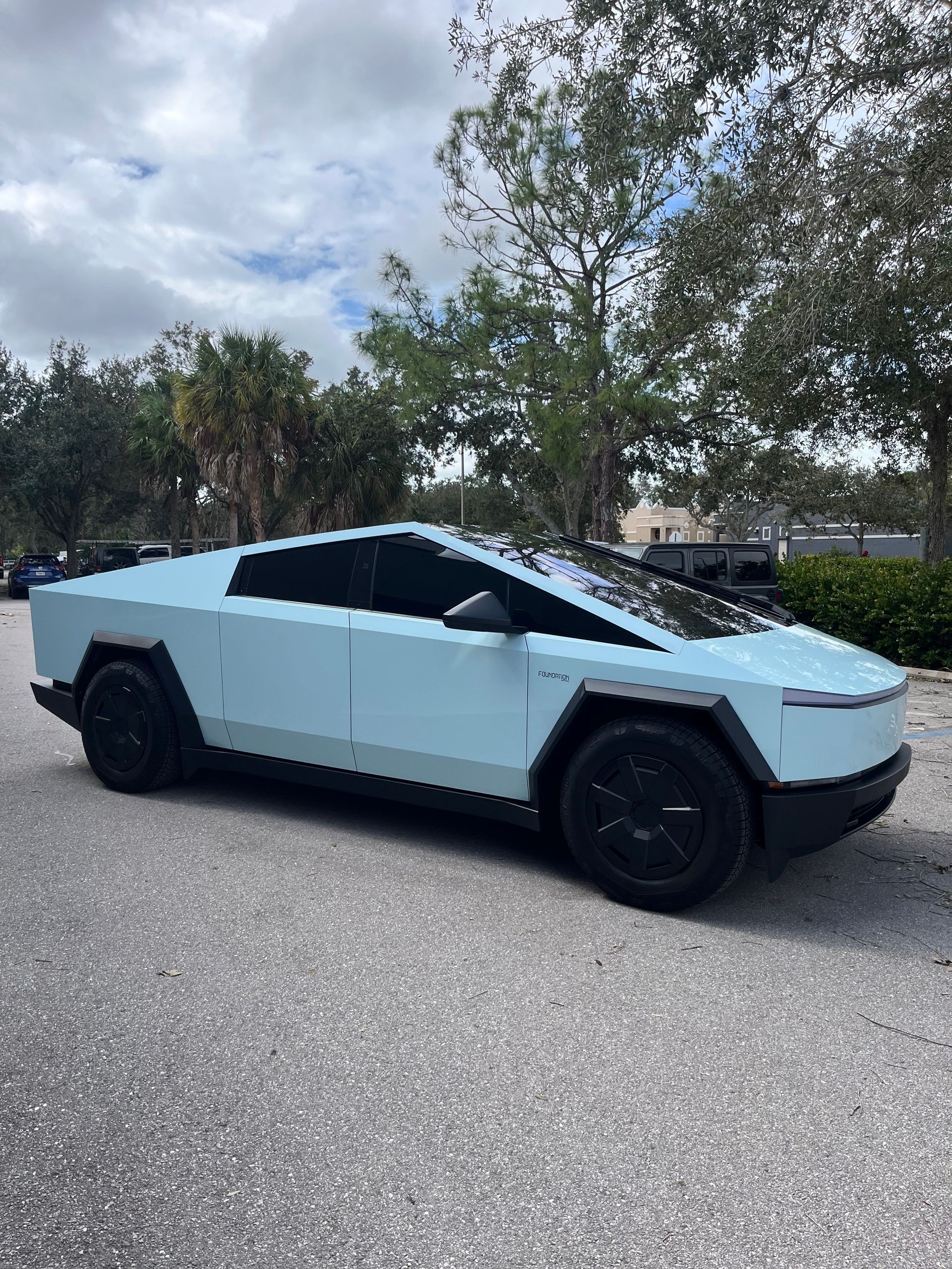 Light blue Tesla Cybertruck parked on a street under cloudy sky