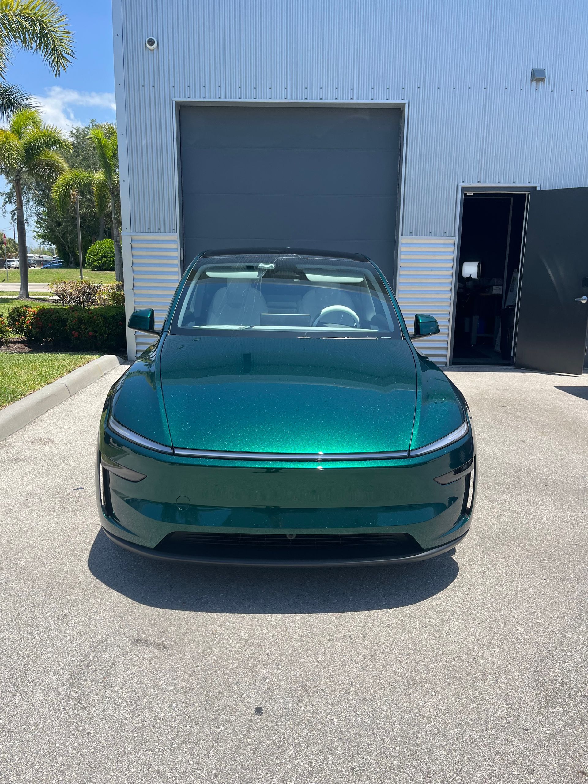 Teal sports car parked in front of a warehouse loading bay on a sunny day