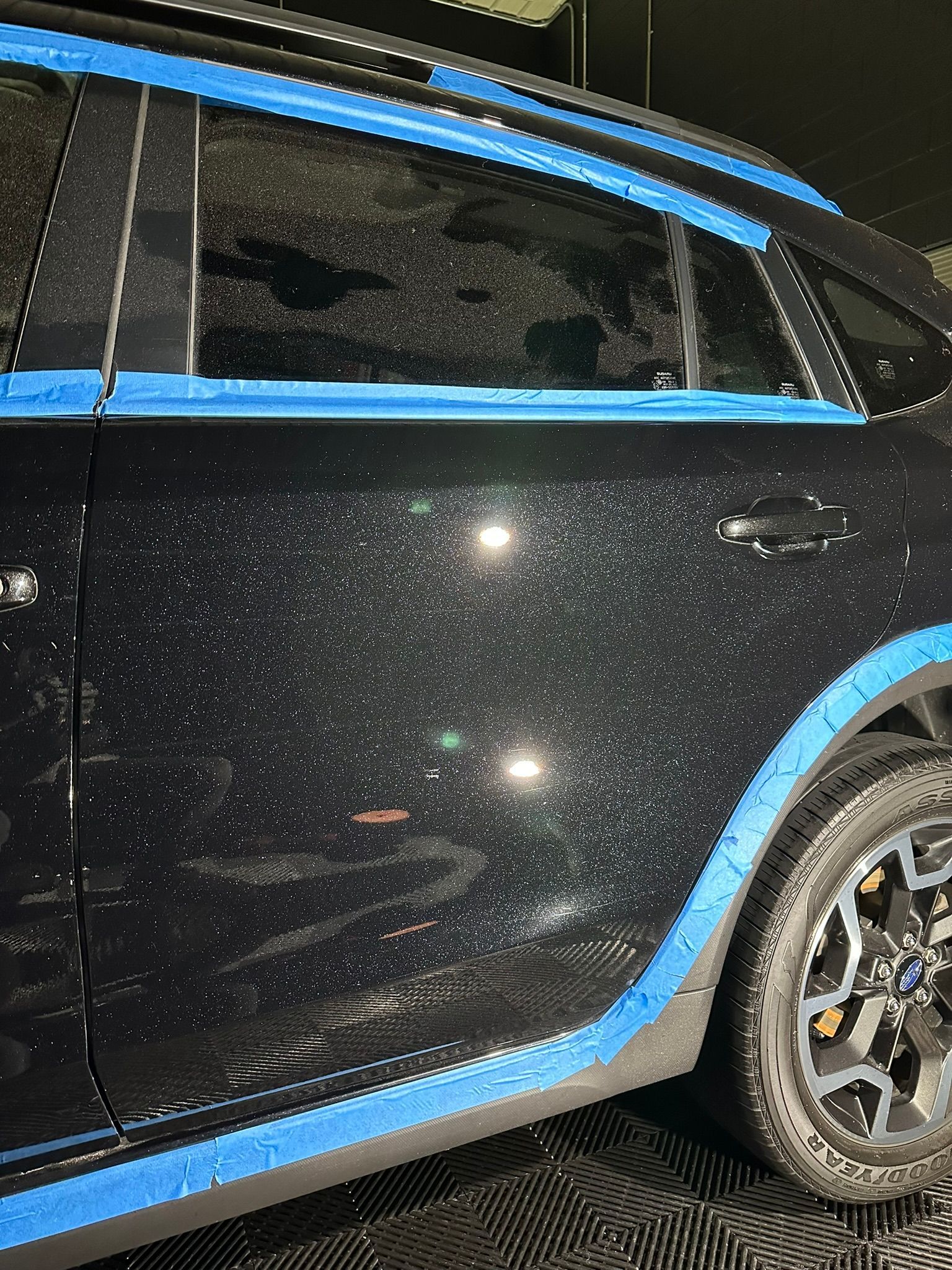 A black car with blue tape on it is sitting on a tiled floor.
