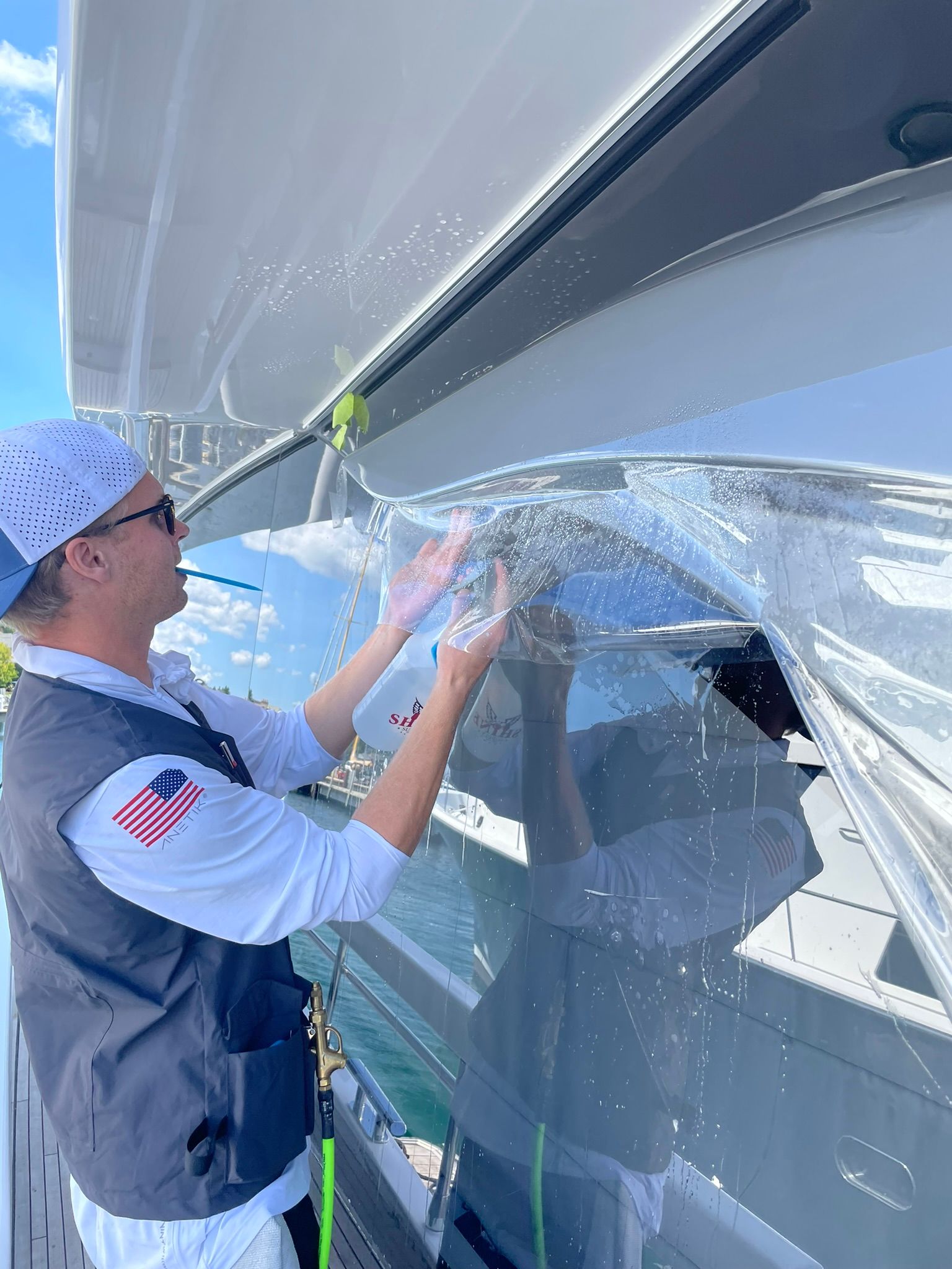 Person in a vest peeling clear protective film from a large white boat hull.