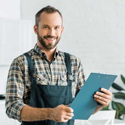 Smiling handyman in apron holding a blue clipboard in a bright workshop